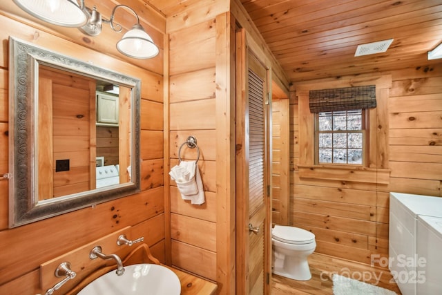 bathroom with wood walls, separate washer and dryer, hardwood / wood-style flooring, wood ceiling, and toilet