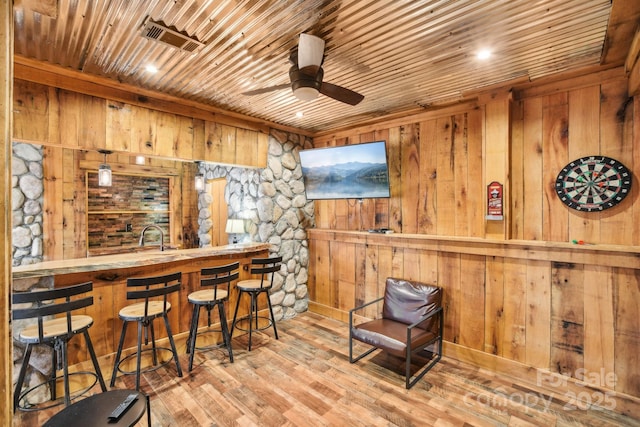 bar featuring wooden walls, wooden ceiling, ceiling fan, and light hardwood / wood-style flooring