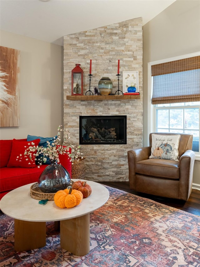 living room with a stone fireplace, hardwood / wood-style floors, and vaulted ceiling