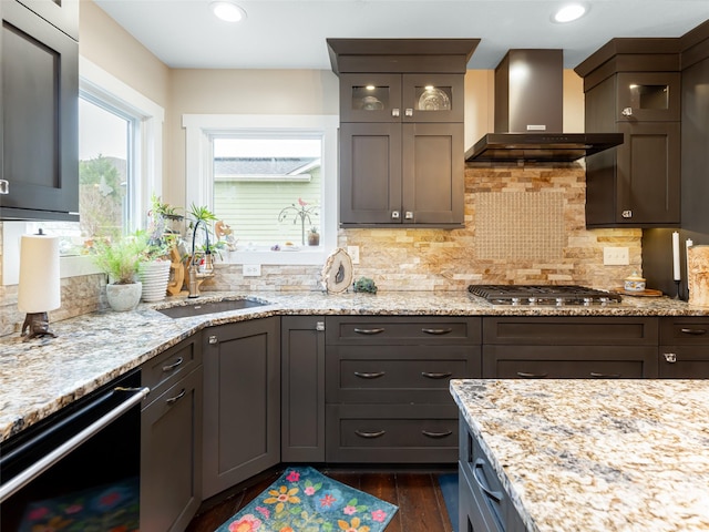 kitchen featuring dishwasher, wall chimney exhaust hood, light stone counters, dark hardwood / wood-style flooring, and stainless steel gas stovetop