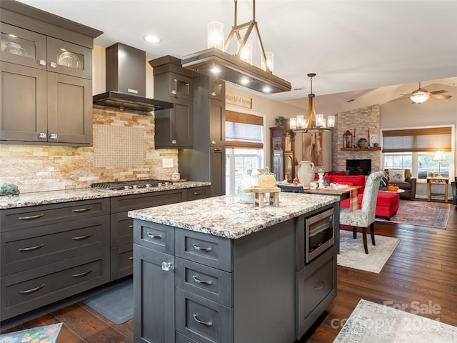 kitchen featuring a fireplace, a healthy amount of sunlight, wall chimney range hood, and hanging light fixtures