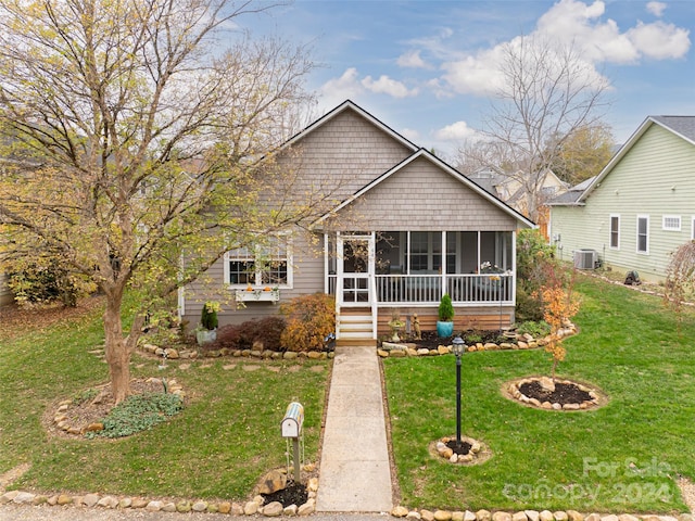 view of front facade featuring central AC, a sunroom, a front lawn, and a fire pit