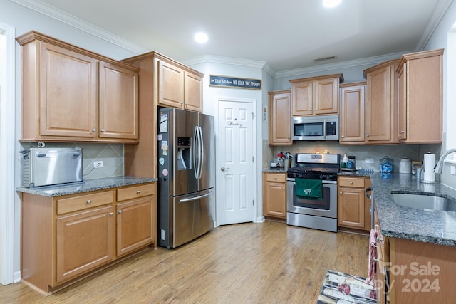 kitchen with ornamental molding, stainless steel appliances, sink, dark stone countertops, and light hardwood / wood-style floors