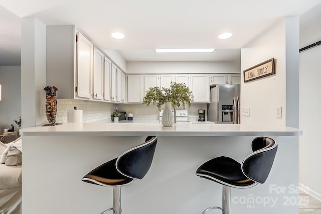 kitchen featuring stainless steel fridge, a breakfast bar area, kitchen peninsula, and white cabinets