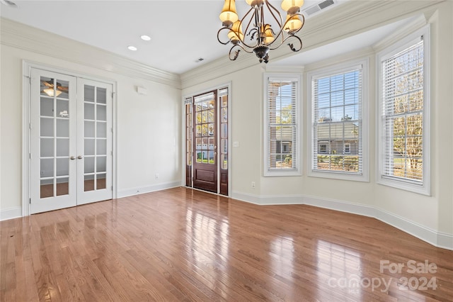 unfurnished dining area featuring hardwood / wood-style floors, a chandelier, french doors, and ornamental molding