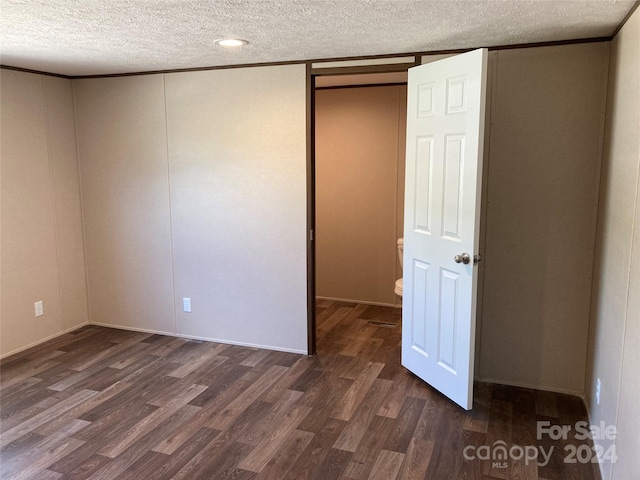 unfurnished bedroom featuring dark wood-type flooring, a textured ceiling, and ornamental molding