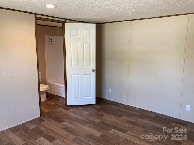 unfurnished bedroom featuring a textured ceiling, dark hardwood / wood-style floors, and ensuite bathroom