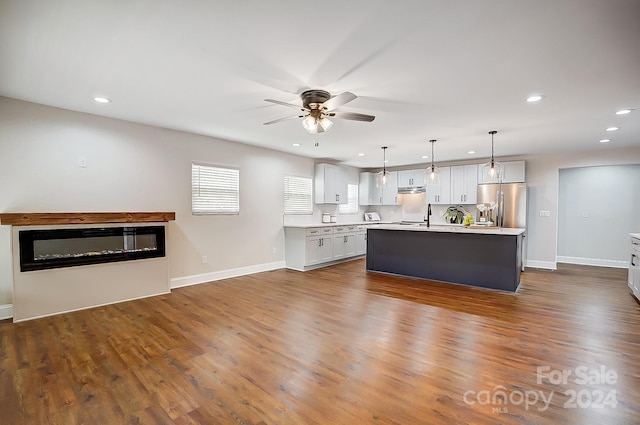 kitchen featuring stainless steel fridge, white cabinets, dark hardwood / wood-style floors, hanging light fixtures, and an island with sink