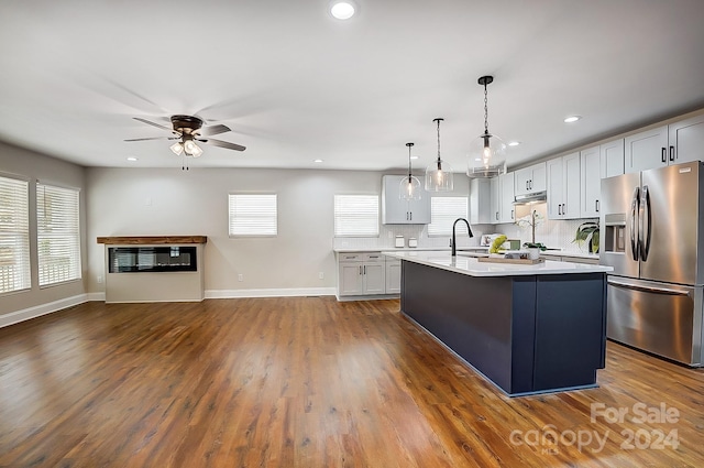 kitchen with stainless steel fridge, an island with sink, decorative light fixtures, and dark hardwood / wood-style floors