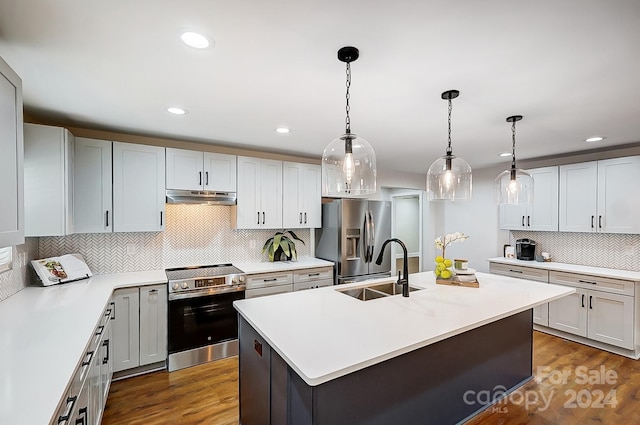 kitchen with pendant lighting, a kitchen island with sink, dark wood-type flooring, sink, and stainless steel appliances