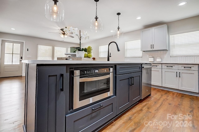 kitchen featuring a center island with sink, stainless steel oven, light wood-type flooring, and hanging light fixtures