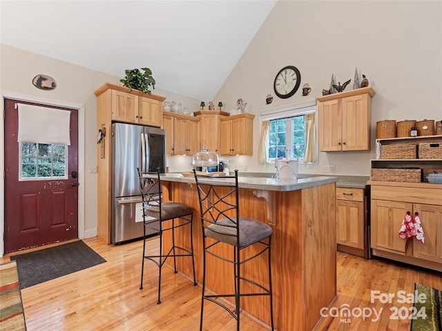 kitchen with a kitchen breakfast bar, stainless steel fridge, a kitchen island, and light hardwood / wood-style flooring