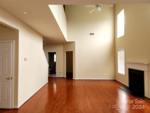 unfurnished living room featuring hardwood / wood-style floors, ceiling fan, and a high ceiling