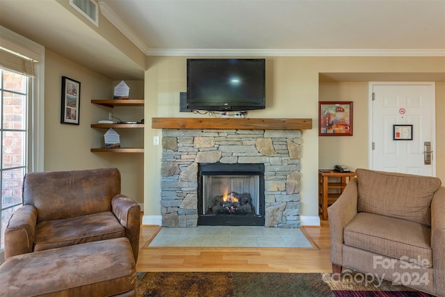 living room featuring hardwood / wood-style floors, a stone fireplace, built in features, and crown molding