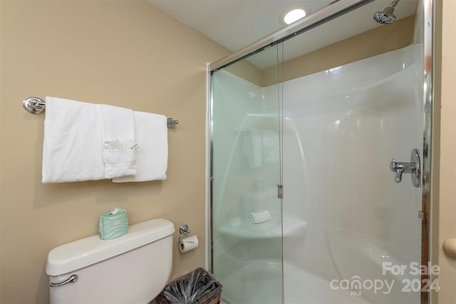 bathroom featuring a shower with door and toilet