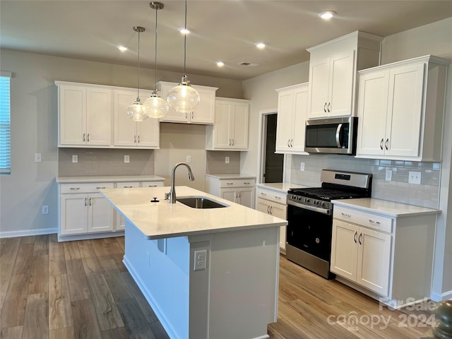 kitchen featuring stainless steel appliances, sink, decorative light fixtures, white cabinets, and an island with sink