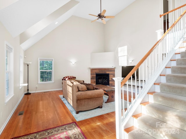 living room with ceiling fan, light hardwood / wood-style floors, a fireplace, and high vaulted ceiling