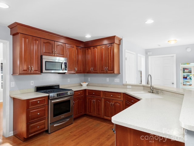 kitchen featuring sink, kitchen peninsula, stainless steel appliances, and light wood-type flooring