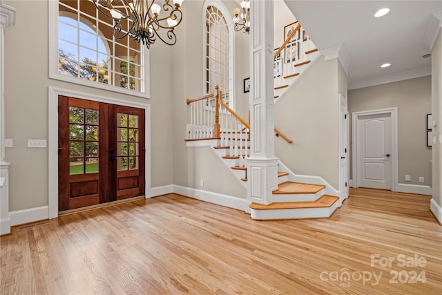 foyer featuring an inviting chandelier, french doors, crown molding, light wood-type flooring, and a towering ceiling