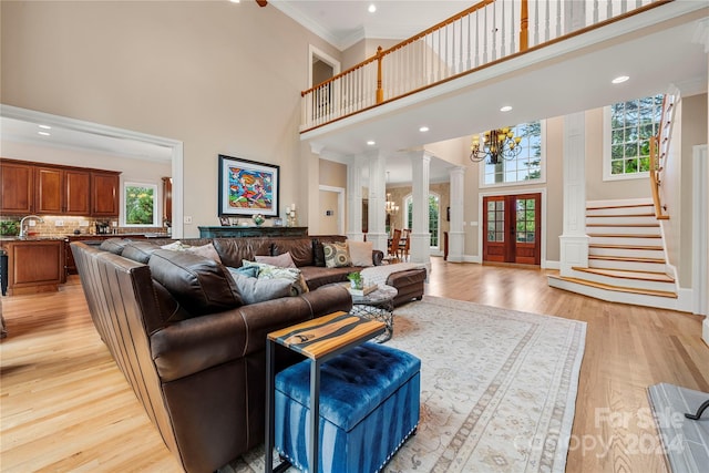 living room with light wood-type flooring, decorative columns, crown molding, a notable chandelier, and a high ceiling