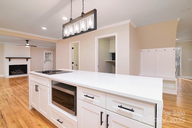 kitchen with pendant lighting, white cabinetry, black electric stovetop, a fireplace, and ceiling fan