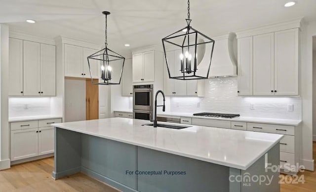 kitchen featuring decorative light fixtures, premium range hood, white cabinetry, and a kitchen island with sink