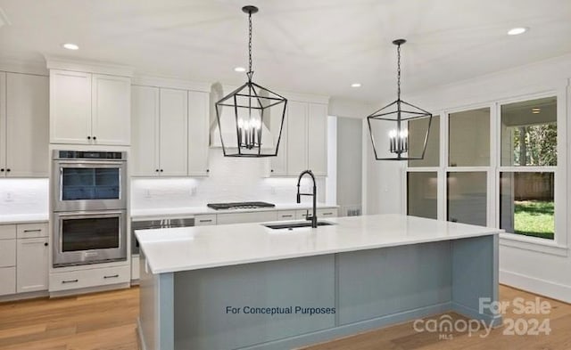 kitchen featuring white cabinetry, hanging light fixtures, light hardwood / wood-style flooring, double oven, and a kitchen island with sink