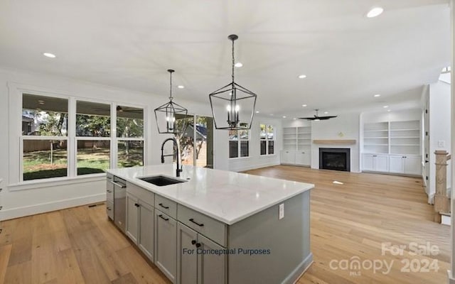 kitchen with a kitchen island with sink, hanging light fixtures, sink, light hardwood / wood-style flooring, and gray cabinets