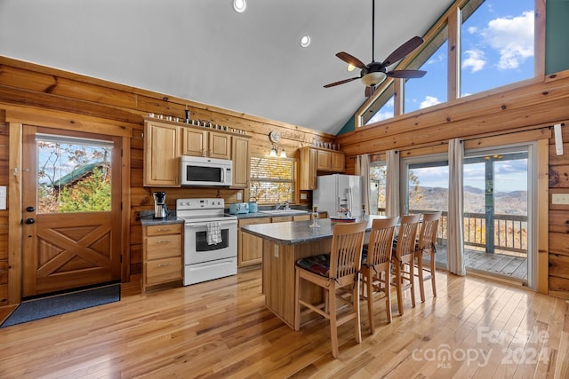 kitchen with white appliances, light hardwood / wood-style flooring, high vaulted ceiling, a kitchen island, and wood walls