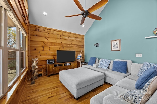 living room featuring light wood-type flooring, high vaulted ceiling, ceiling fan, and wood walls