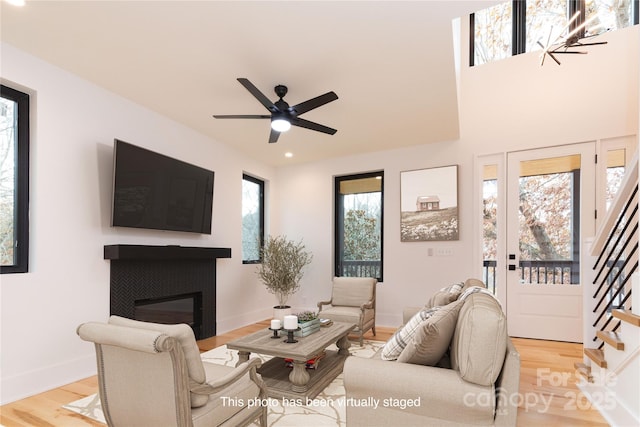 living room with a tiled fireplace, ceiling fan, and light hardwood / wood-style flooring