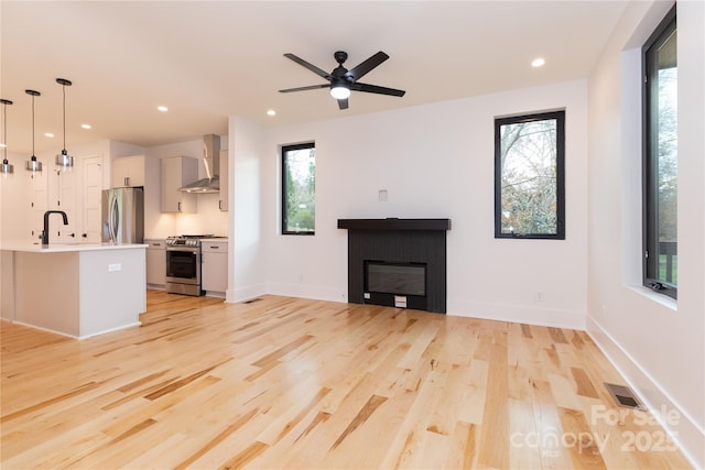 unfurnished living room with a tiled fireplace, a wealth of natural light, ceiling fan, and light hardwood / wood-style flooring