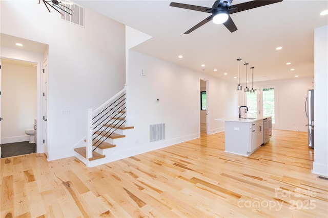 kitchen featuring sink, decorative light fixtures, a center island with sink, light wood-type flooring, and stainless steel fridge