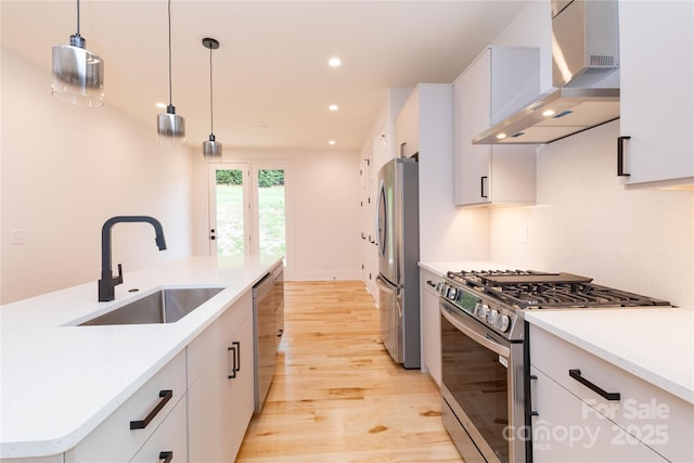 kitchen featuring decorative light fixtures, sink, white cabinets, stainless steel appliances, and wall chimney exhaust hood