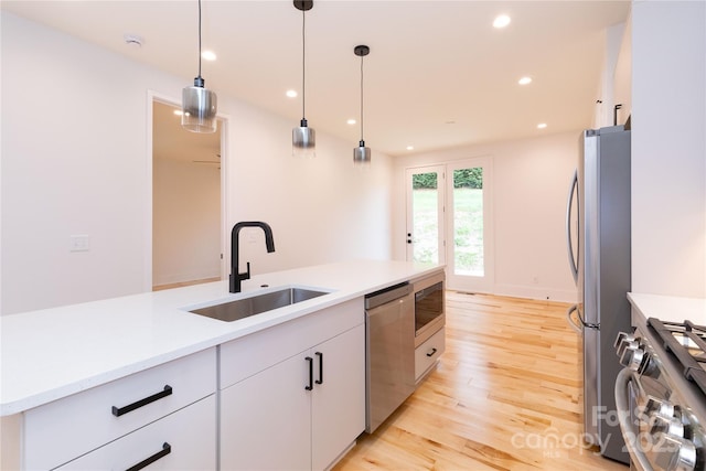 kitchen with sink, white cabinetry, hanging light fixtures, stainless steel appliances, and light hardwood / wood-style floors