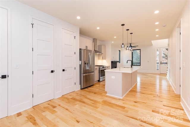 kitchen featuring appliances with stainless steel finishes, a kitchen island with sink, white cabinetry, decorative light fixtures, and wall chimney exhaust hood