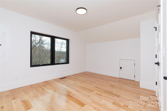 empty room with light hardwood / wood-style floors and vaulted ceiling