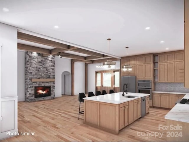 kitchen with a kitchen island with sink, a stone fireplace, sink, beamed ceiling, and light hardwood / wood-style floors