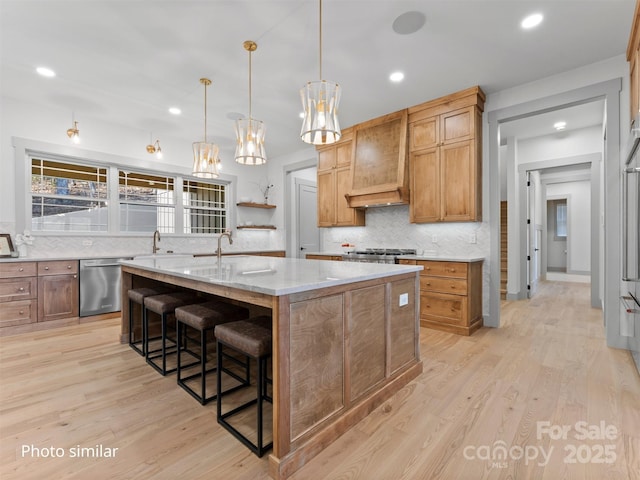 kitchen featuring brown cabinets, custom range hood, a kitchen island with sink, dishwasher, and a kitchen breakfast bar