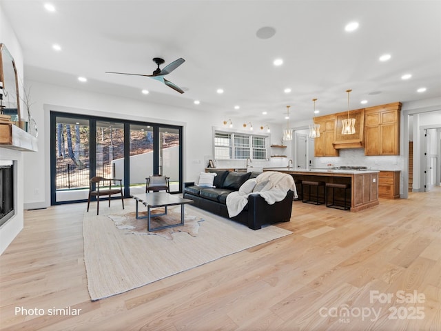 living area with a ceiling fan, light wood-type flooring, a glass covered fireplace, and recessed lighting