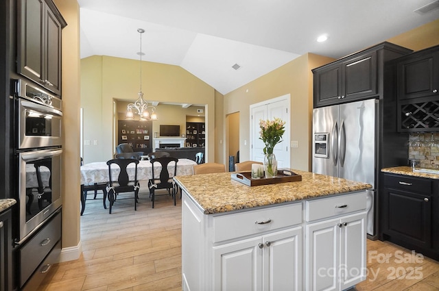 kitchen with lofted ceiling, white cabinets, light hardwood / wood-style floors, appliances with stainless steel finishes, and a kitchen island