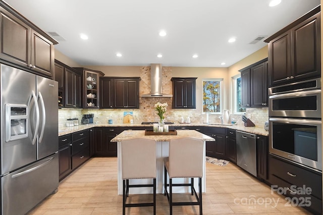 kitchen with appliances with stainless steel finishes, a kitchen breakfast bar, tasteful backsplash, wall chimney exhaust hood, and a center island