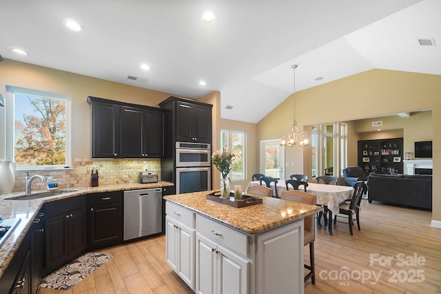 kitchen featuring white cabinetry, a notable chandelier, vaulted ceiling, a kitchen island, and appliances with stainless steel finishes