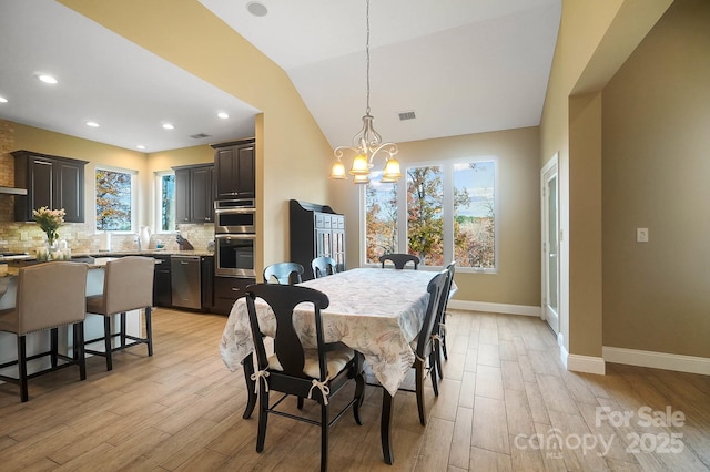 dining room with light hardwood / wood-style floors, vaulted ceiling, a notable chandelier, and sink