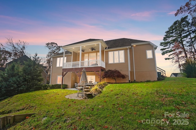 back house at dusk featuring a lawn and ceiling fan