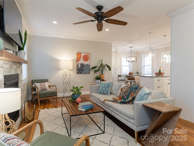 living room featuring ornamental molding, a fireplace, ceiling fan with notable chandelier, and light wood-type flooring