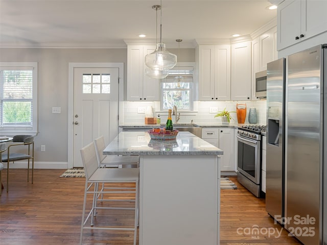 kitchen featuring a kitchen island, decorative light fixtures, white cabinetry, stainless steel appliances, and light stone countertops