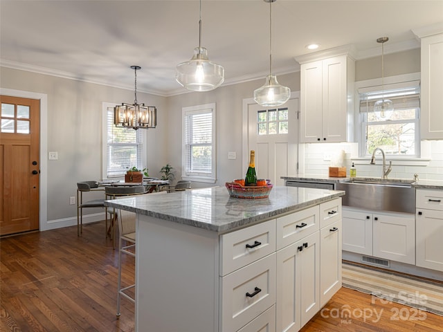 kitchen with sink, white cabinets, hanging light fixtures, a center island, and light stone counters