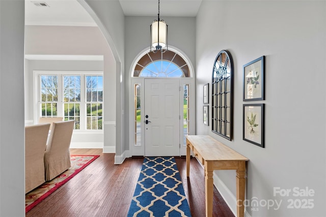 foyer featuring arched walkways, dark wood-style flooring, visible vents, a high ceiling, and baseboards