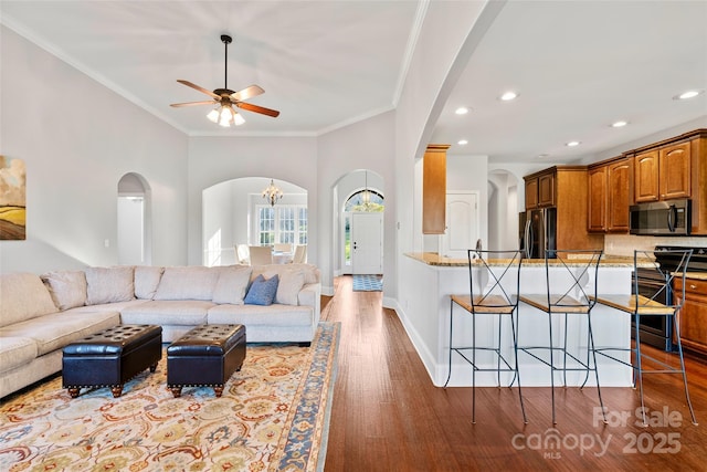 living room with crown molding, recessed lighting, wood finished floors, baseboards, and ceiling fan with notable chandelier